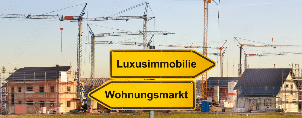 Obraz premium Vor einem Neubaugebiet mit vielen Baustellen und Baukränen steht ein Wegweiser mit der Aufschrift Luxusimmobilie vs. Wohnungsmarkt - FOTOMONTAGE