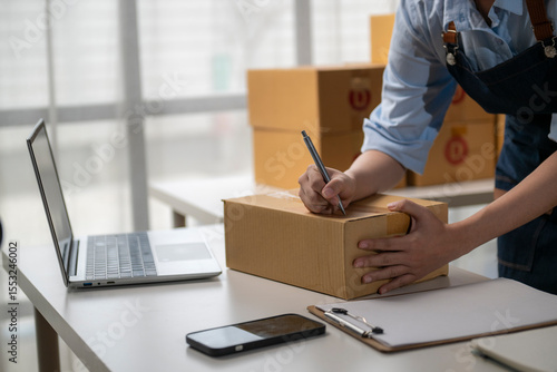 Foto Online seller writing customer address on cardboard box, preparing ecommerce par
