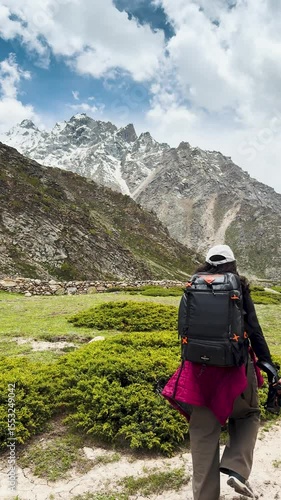 4K Vertical video of teenager backpacker girl hiking in mountains during summer season. Green meadows and cloudy sky in Himalayas.
