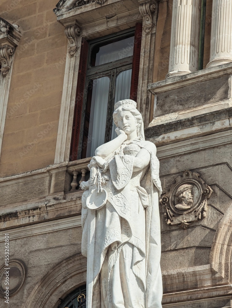 Fototapeta premium Elegant stone statue of a woman in intricate attire against a historic building facade in Bilbao.