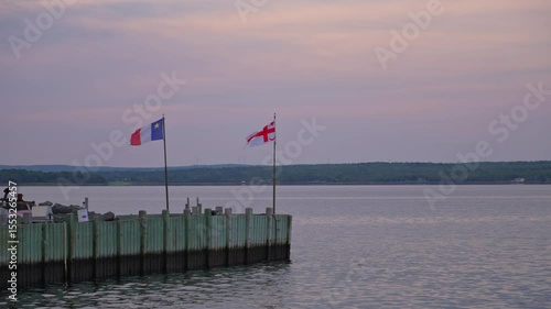 Sunrise over harbor with Acadian and Mikmaq flags waving gently