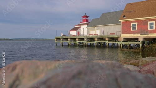 Rocks in foreground with sunrise view of wharf lighthouse and harbor water
