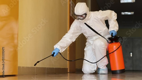 Professional pest control technician in protective hazmat gear sprays disinfectant solution across building floor. Targeting harmful microorganisms
