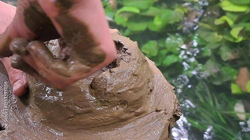 Sensory play in nature: A child discovers the texture of mud, sculpting a simple pot from clay found by a river. Handheld close-up shot.