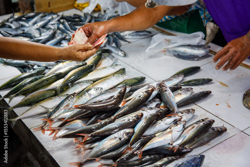 Buying fresh fish at wet market in Philippines with vendor receiving money over display of seafood on white tiles