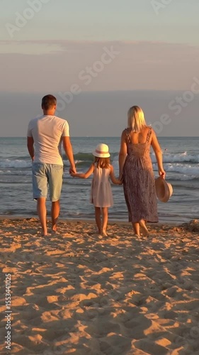 Back view of happy family walk on sand beach at sea at sunset. Father mother and little daughter on summer vacation.Travel holiday. Vertical shot