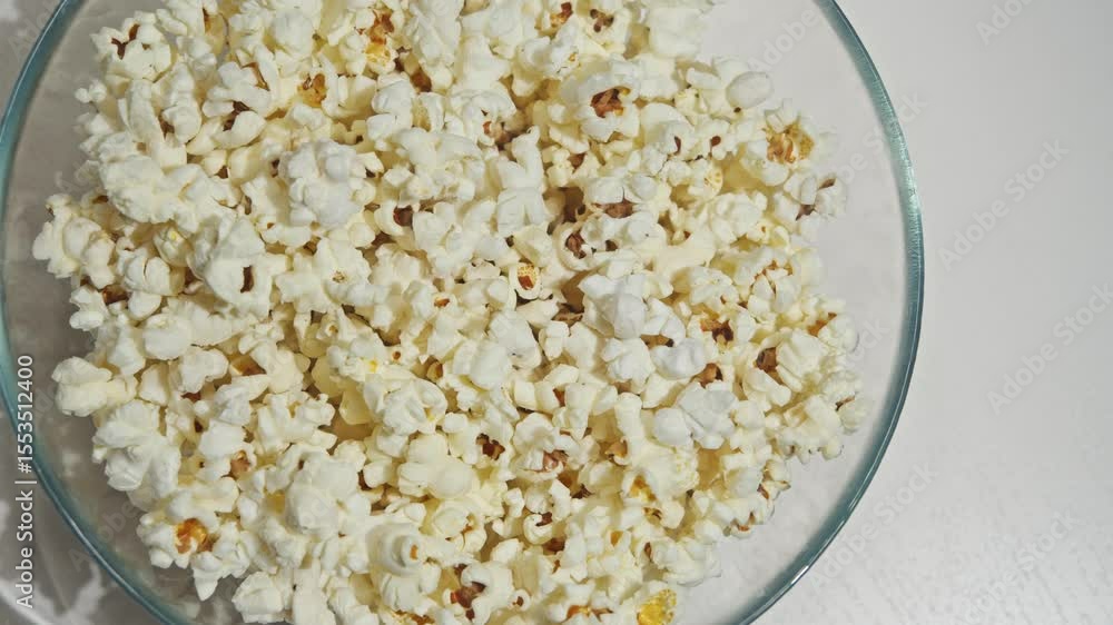 man's hand takes a handful of caramel popcorn from a large glass vase standing on a white coffee table. Top view man's hand takes a handful of caramel popcorn from a large glass vase standing on a white coffee table. Top view