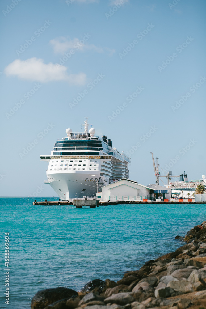 Naklejka premium Large cruise ship docked at harbor with vibrant blue waters and rocky shoreline under a clear sky