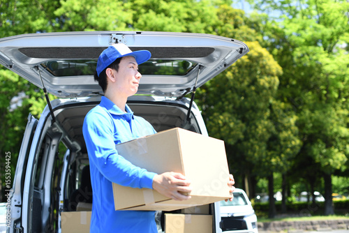 軽バンの前で荷物を運ぶアジア人男性配達員