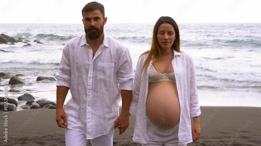 Happy young couple walking on the beach and kissing each other in front of camera - Love, pregnancy and parenthood concept  