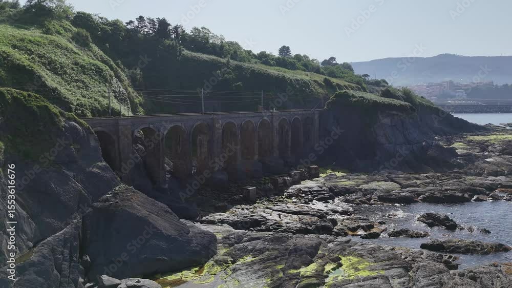 Pont en pierre à arches romaines et voie ferrée en bord d’océan à Bermeo, drone