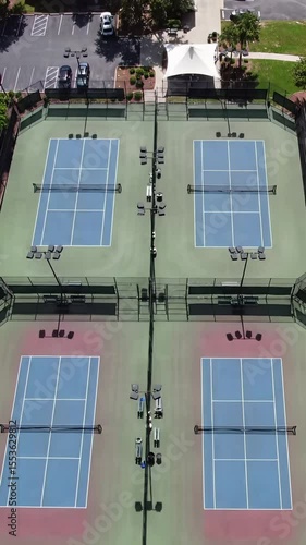 aerial vertical pan video over vibrant outdoor sports courts including blue/green tennis courts and red/blue pickleball court, showing fences & benches, tilting towards white sky. Dynamic aerial
