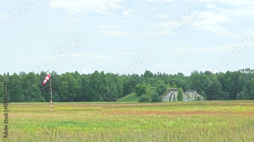 Two closed bunkers for army air-craft and red white windsock moving in the air. Closed defence airport without army.