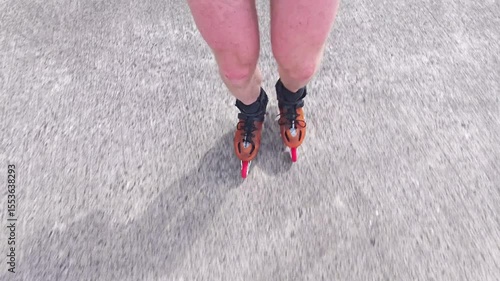 Close-up view of male legs in orange inline blades boots moving on the road. 