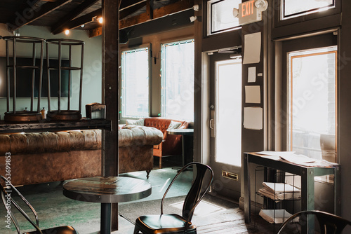 Canvas-taulu Sunlit rustic café interior with tufted leather sofa, industrial metal chairs, r
