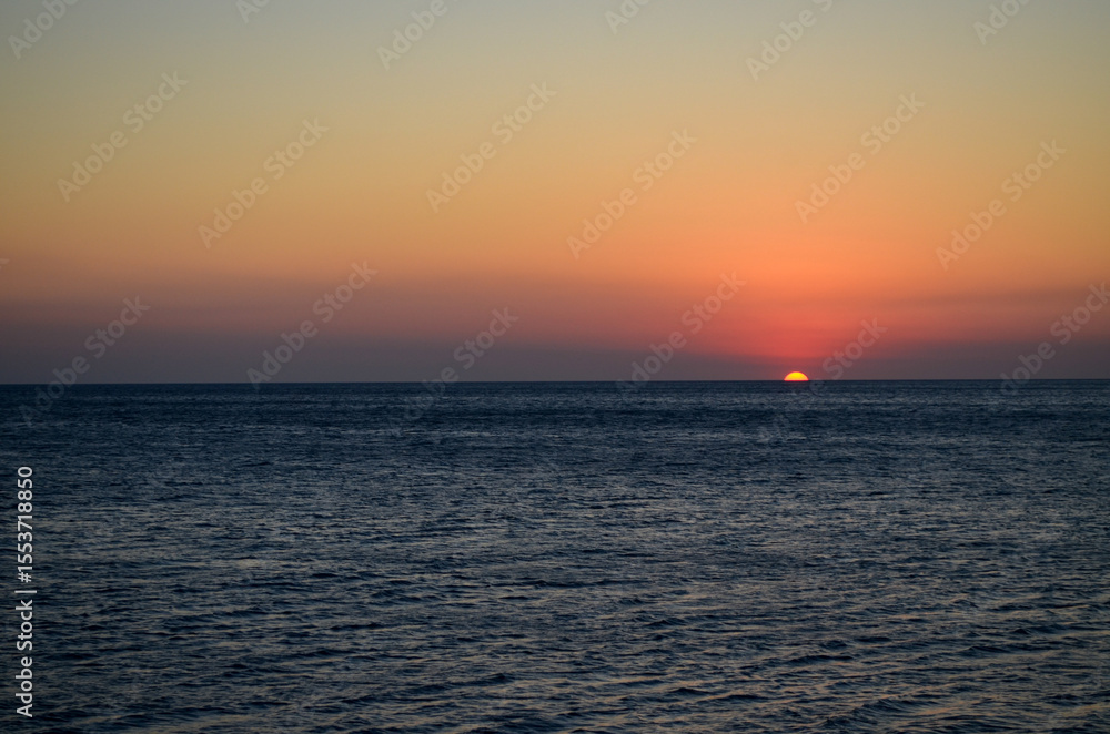Fototapeta premium The ocean is calm and the sky is a beautiful orange color. The sun is setting, creating a warm and peaceful atmosphere