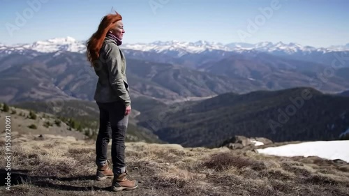Woman standing on snowy mountain peak overlooking vast mountain landscape