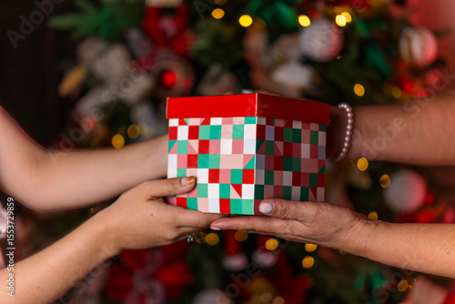 Hands Exchanging a Christmas Gift Box in Front of Decorated Tree