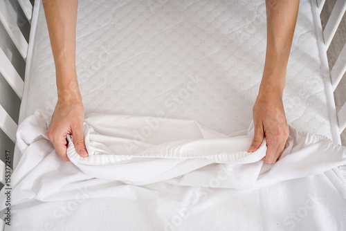 Young woman?s hands putting fitted sheet on baby crib mattress.