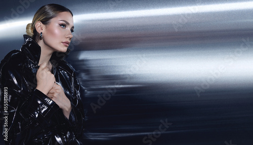Fashion model in black leather trench coat and thigh-high boots posing in futuristic, metallic interior. Elegant editorial fashion photoshoot with dramatic lighting.
