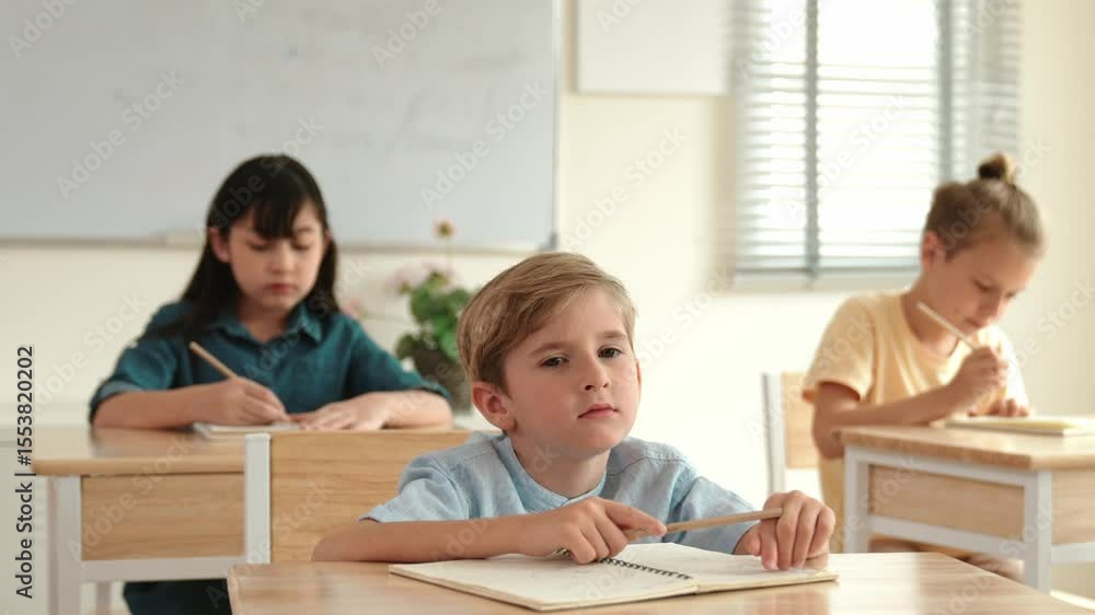 Caucasian boy looking at blackboard while diverse skilled student learning at school and taking a note. Smart child in casual cloth sitting in front of blackboard while children doing test. Pedagogy. Caucasian boy looking at blackboard while diverse skilled student learning at school and taking a note. Smart child in casual cloth sitting in front of blackboard while children doing test. Pedagogy.
