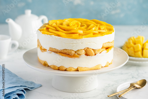 Round whole tiramisu cake with mango on a stand on a marble table. Famous Italian dessert with tropical fruits. Selective focus