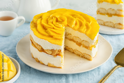 Round tiramisu cake with mango on a plate on a blue tablecloth. Variation of the Italian dessert with exotic fruit. Selective focus
