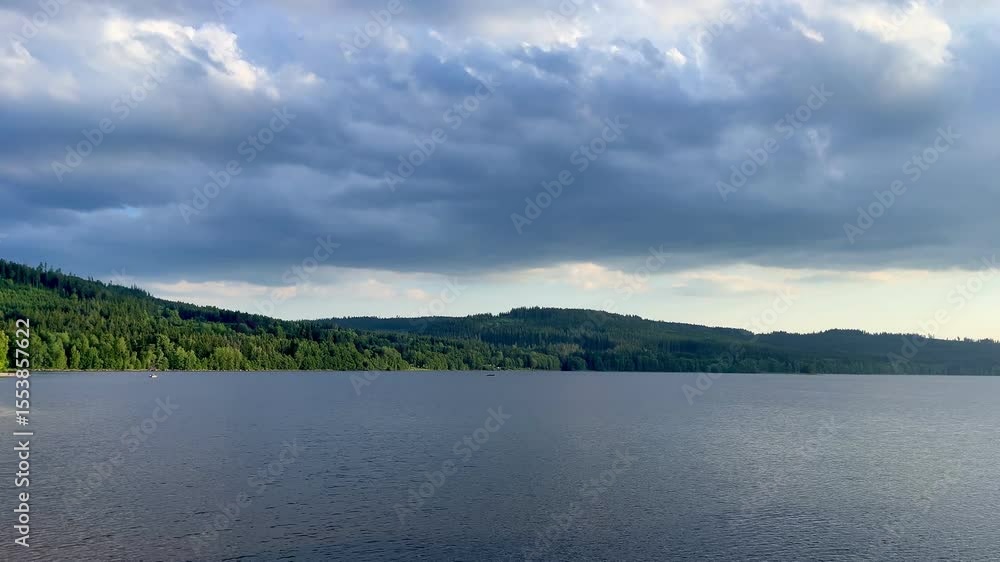 Wide static shot of still lake surrounded by forested hills under cloudy sky. Tranquil mood and natural landscape, perfect for atmospheric footage. Wide static shot of still lake surrounded by forested hills under cloudy sky. Tranquil mood and natural landscape, perfect for atmospheric footage.