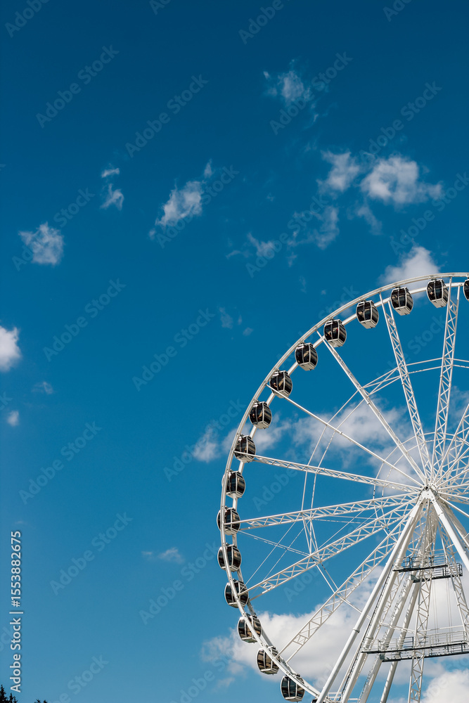Fototapeta premium Ferris wheel turns against a bright blue sky in a lively amusement park setting