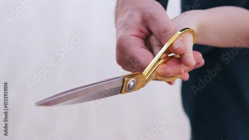 Close-up of golden scissors as an adult and a child cut a red ribbon together, symbolizing a meaningful moment, intergenerational unity, and the ceremonial nature of the event
