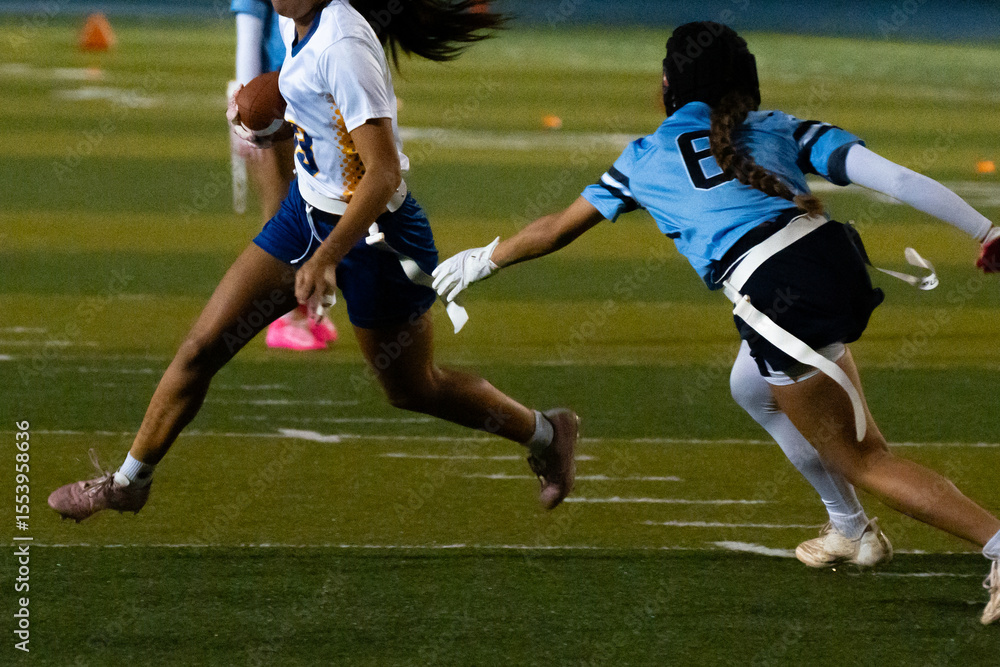 Close-up of intense flag football play, girl sprinting with ball as opponent lunges to grab flag, dynamic youth sports action, girls in motion, athletic energy, competition and pursuit on turf. Close-up of intense flag football play, girl sprinting with ball as opponent lunges to grab flag, dynamic youth sports action, girls in motion, athletic energy, competition and pursuit on turf.