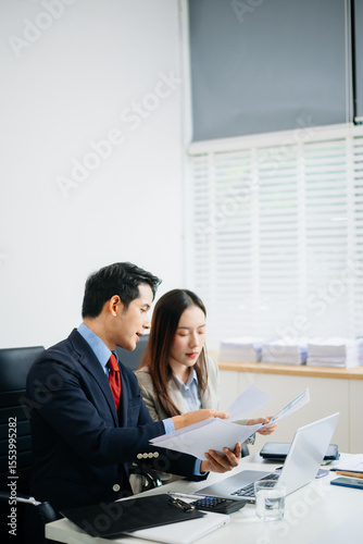 Wallpaper Mural Two Asian professionals reviewing financial charts together in a modern office. Business, teamwork, analytics, strategy Torontodigital.ca