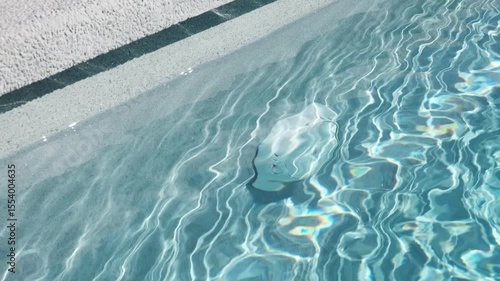 Underwater section of a swimming pool with clear blue water and an integrated plastic circulation system element. Bright sunlight reflections create a vibrant light pattern on the water
