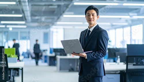 A Korean man in a suit holding a laptop computer to the right, with luxury office furniture in the blurred background