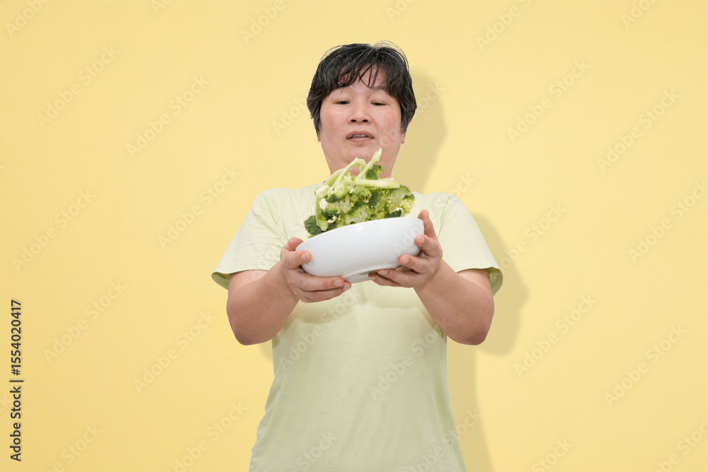 middle aged asian woman overflowing raw broccoli in studio background