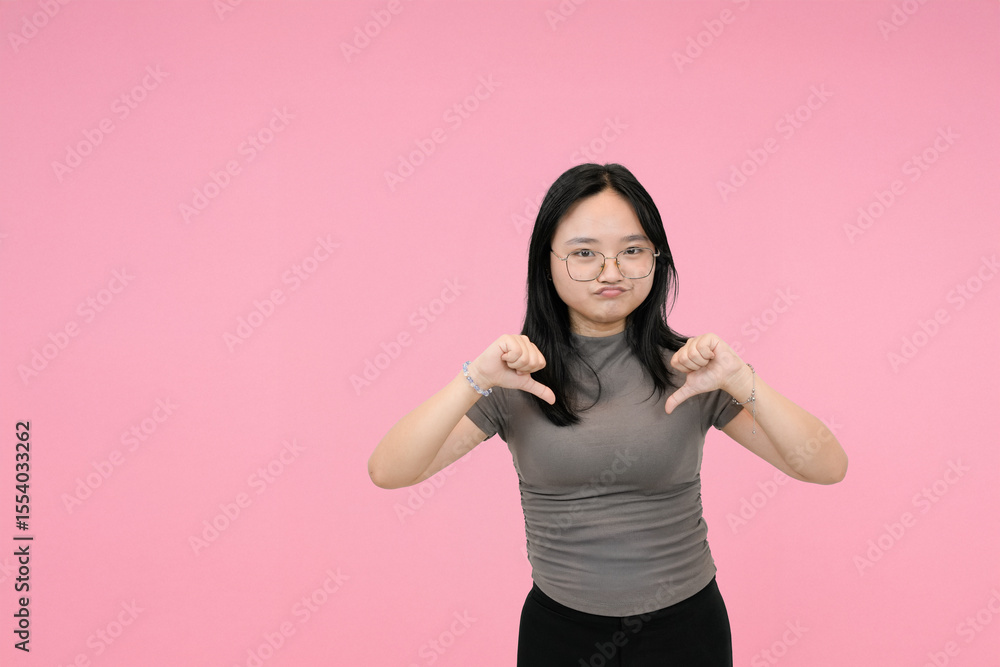 short asian woman giving thumbs down showing disagreement in studio background short asian woman giving thumbs down showing disagreement in studio background