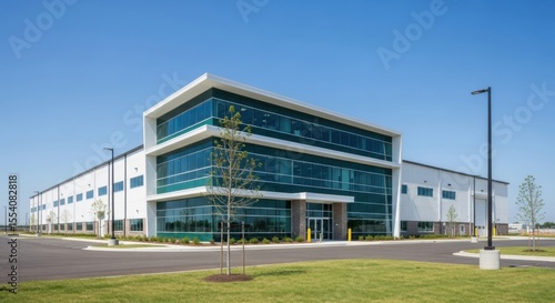Modern Industrial Warehouse Building with Contemporary Office Facade Featuring Large Glass Windows and Clean Architectural Lines Under a Clear Blue Sky
