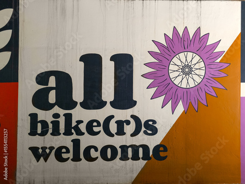 Inclusive Urban Mural Saying ‘All Bikers Welcome’ with Stylized Bike Flower Design

