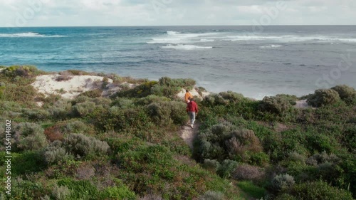 Wallpaper Mural Two young adults stroll peacefully along a sandy coastline, surrounded by lush vegetation. Atmosphere of the ocean and dunes creates a calming experience in nature. Torontodigital.ca
