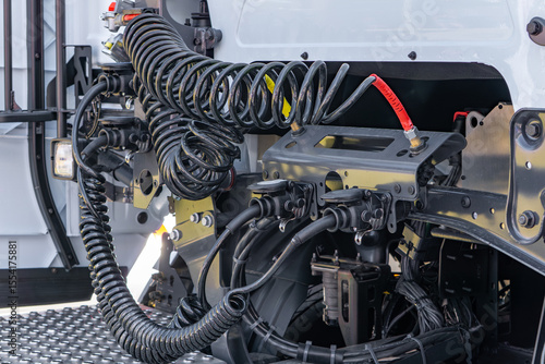view of the rear cab area of a semi-truck, featuring coiled air hoses, electrical wiring, and trailer connection ports. Modern truck coupling system.