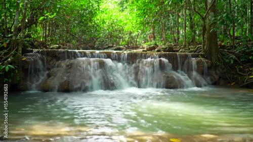 Slow-motion 4K video of a small waterfall cascading into a crystal-clear pool in a tropical jungle, lush greenery around, sunlight filtering through leaves, peaceful and looping background.