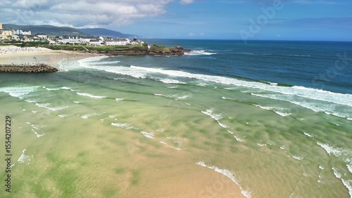 An aerial view captures vibrant waves crashing on sandy beaches under a blue sky, evoking adventure and tranquility