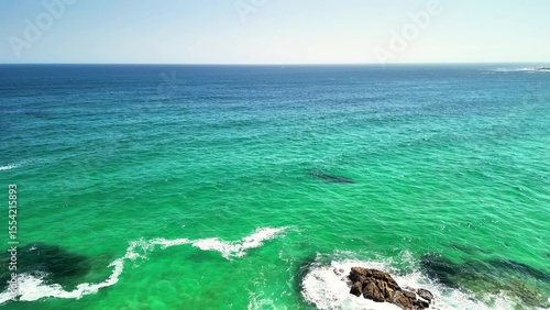 Breathtaking aerial footage of a vibrant turquoise ocean meeting rugged rocks and a sunny coastline.