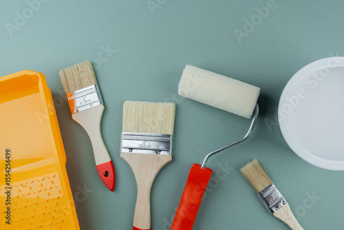 Fototapeta Naklejka Na Ścianę i Meble -  Scattered paint tools with roller, brushes, tray and bucket on green background for interior renovation and DIY project concept