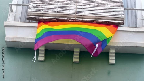 Rainbow pride flag fluttering on residential balcony, representing community solidarity and personal expression