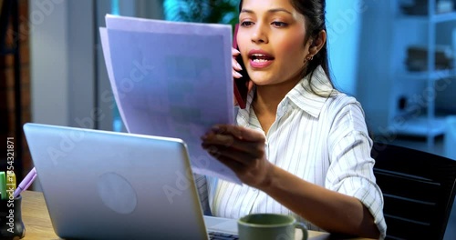 Businesswoman attending phone call with documents at desk in modern cozy office, Indian Asian female holding reports while communicating on mobile during office hours with confident expression