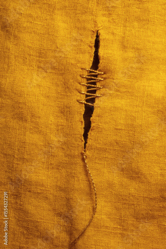 Mended Fabric: A tear in golden-yellow textile is repaired with visible stitching, creating a unique texture and emphasizing the repair.
