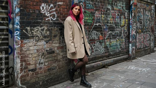 Young Woman Poses Stylishly Beside Colorful Graffiti Wall in Urban Alleyway