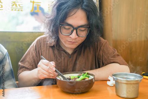 Photography Two young Chinese men in their early twenties, both wearing glasses, are eating lunch together at a Taiwanese restaurant, enjoying a casual spring afternoon in Huangpu District of Shanghai, China