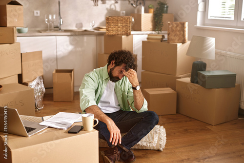 Tableau sur toile A man sits on a rug surrounded by unpacked boxes in his new house